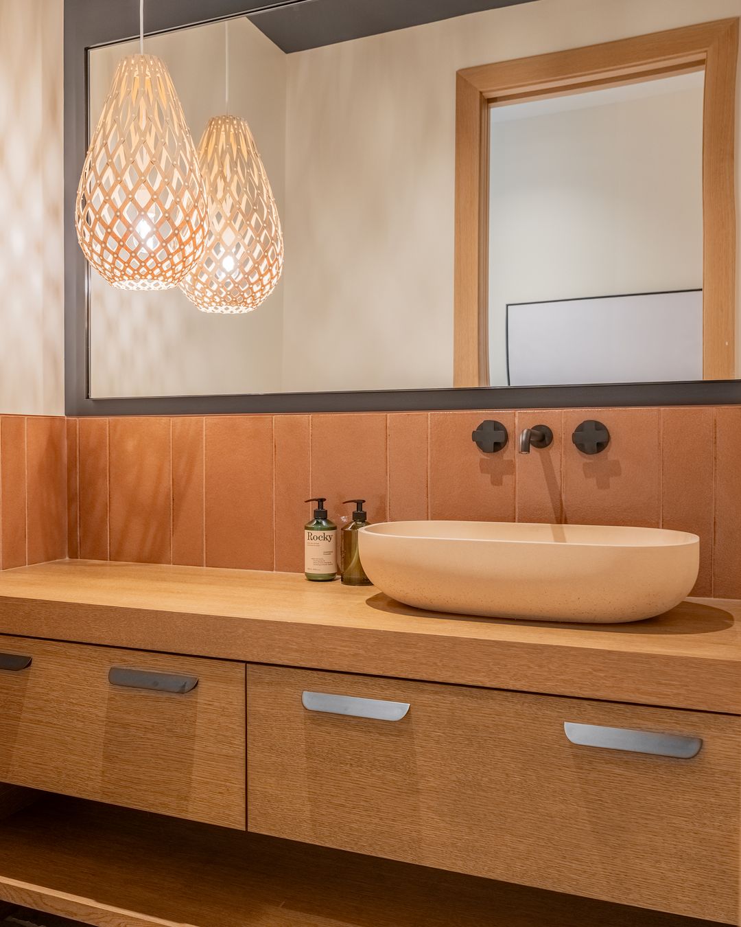 A bathroom vanity under two woven pendants