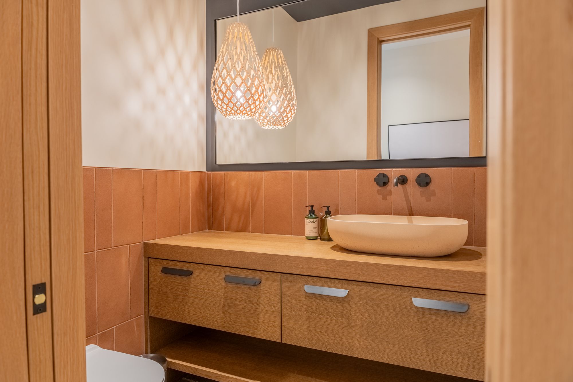 A bathroom vanity under two woven pendants