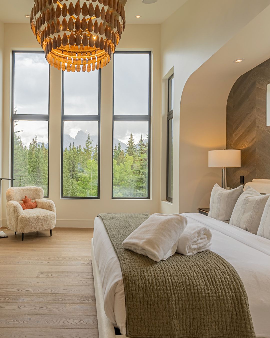A bedroom with tall windows to the forest and the peaks
